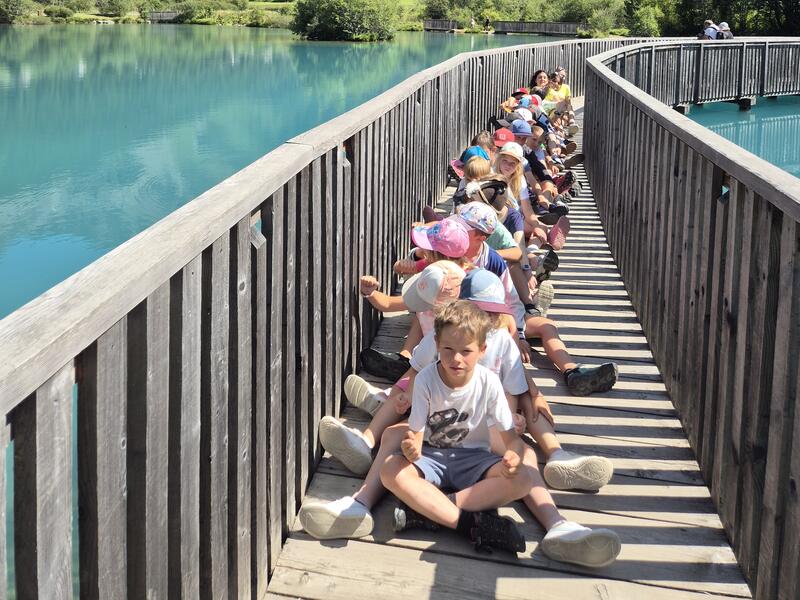 Kindergruppe auf dem Holzsteg über einem Bergsee, dahinter die Berge